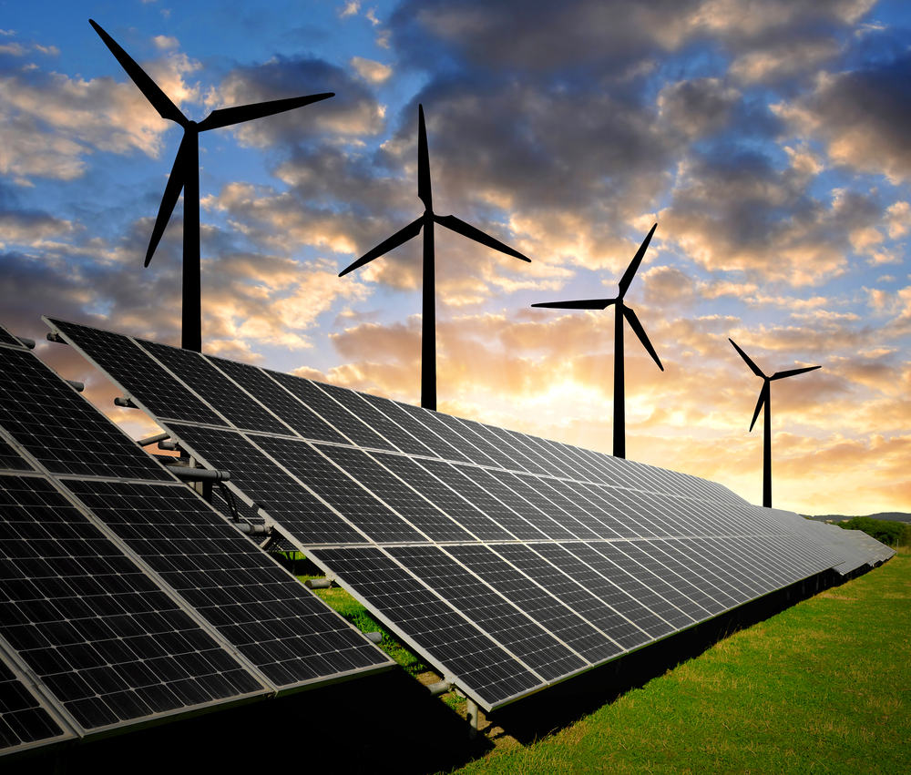 Wind turbines above a grid of solar panels on a green field