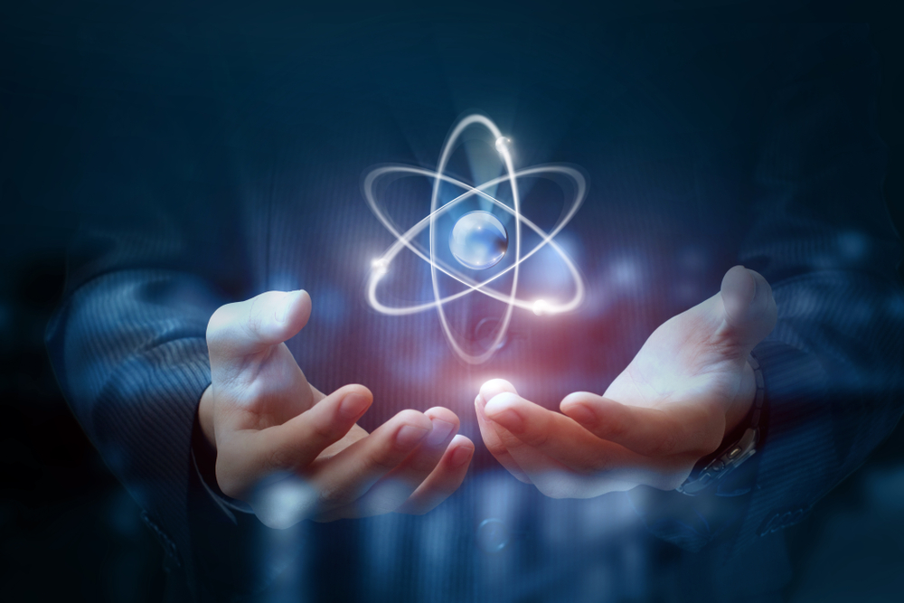Large atom hovering above a pair of hands on a dark blurred background